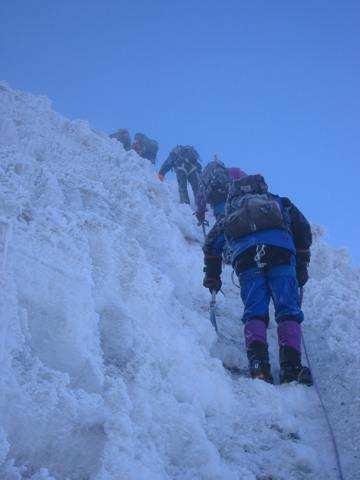 English Ref: mountaineers are climbing a very steep icy slope MLM: a man is standing on a grey rock in the foreground German Ref: bergsteiger klettern auf einen sehr steilen eishang MLM: ein