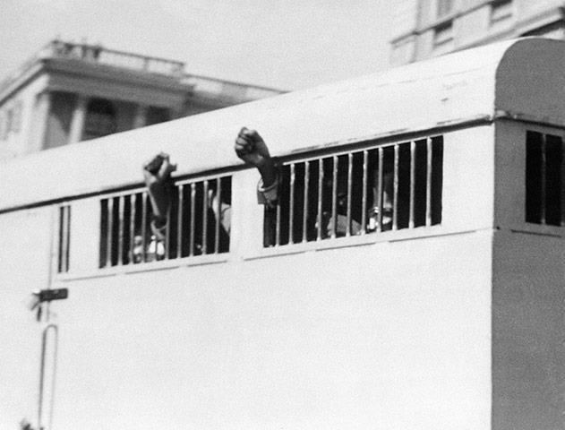 1964: Eight men, among them Nelson Mandela, with their fists raised in defiance through the barred windows of the prison